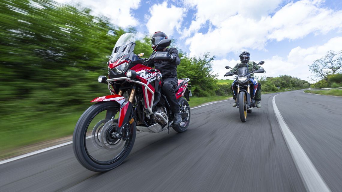 Two riders on adventure motorbikes cruising down a winding asphalt road equipped with MICHELIN Anakee Adventure 2 tyres.