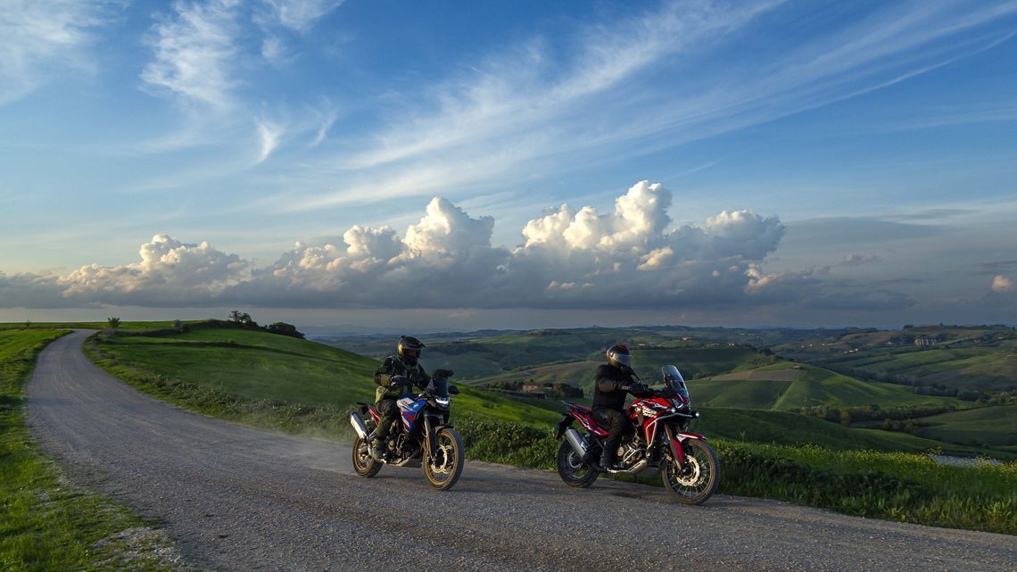 Two riders on adventure motorbikes driving down a scenic dirt road with MICHELIN Anakee Adventure 2 tyres