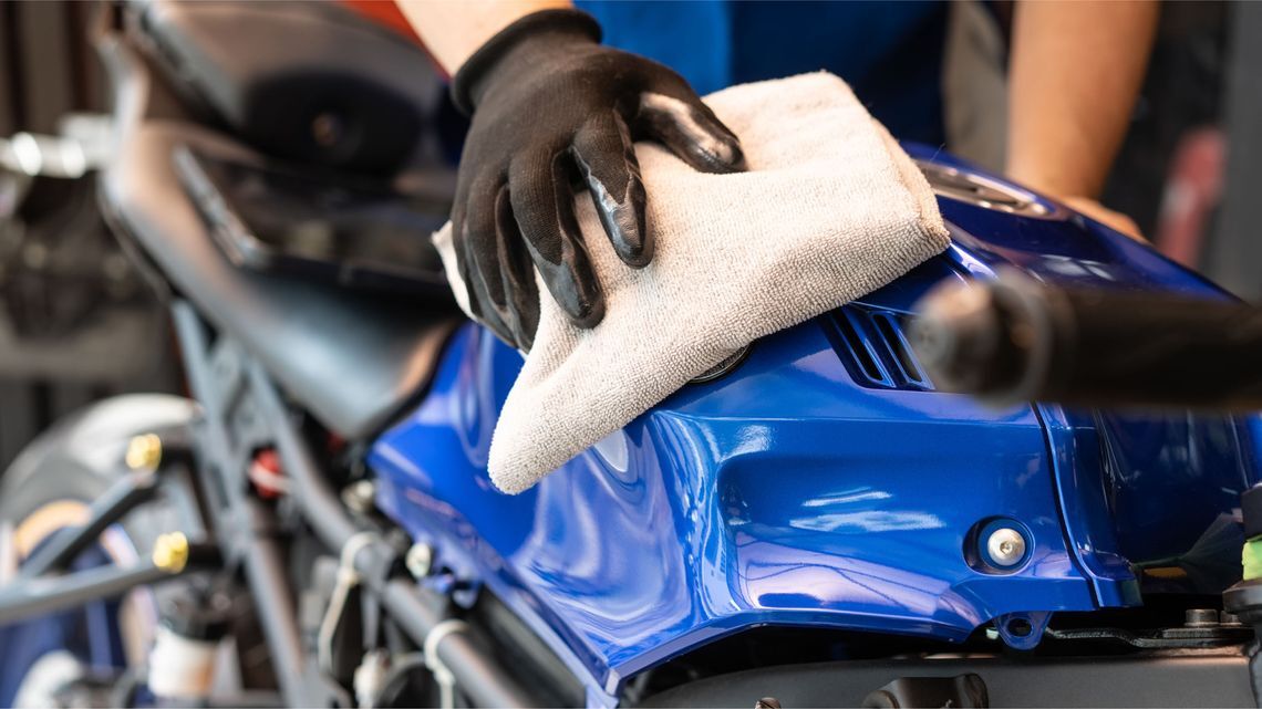 A person cleans a blue motorcycle, ensuring it is free of dirt and debris before winter storage to prevent corrosion