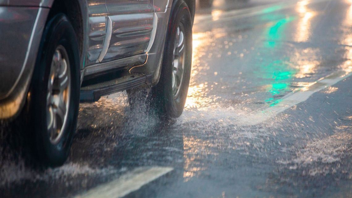 An image of a car’s wheels splashing through water on wet road, monsoon driving.