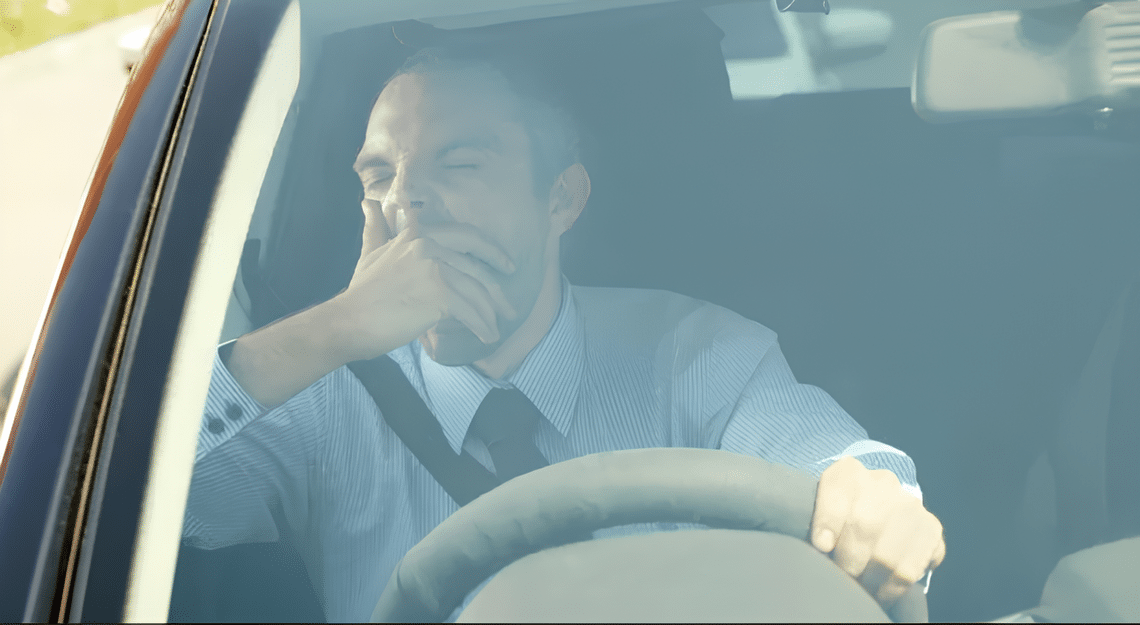 a driver yawning with one hand on the steering wheel