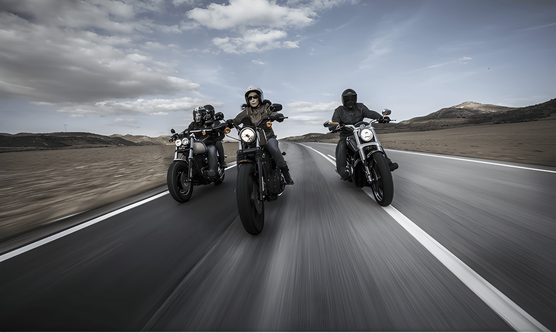 Three motorcyclists ride side by side on an open road under a vast sky. The scene conveys speed, freedom, and adventure in a desert landscape.