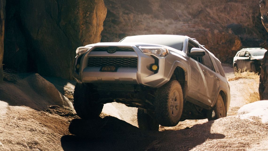 渓谷の岩場を横切る2台のSUV。1台は手前の岩を登り、もう1台は未舗装路を進む。