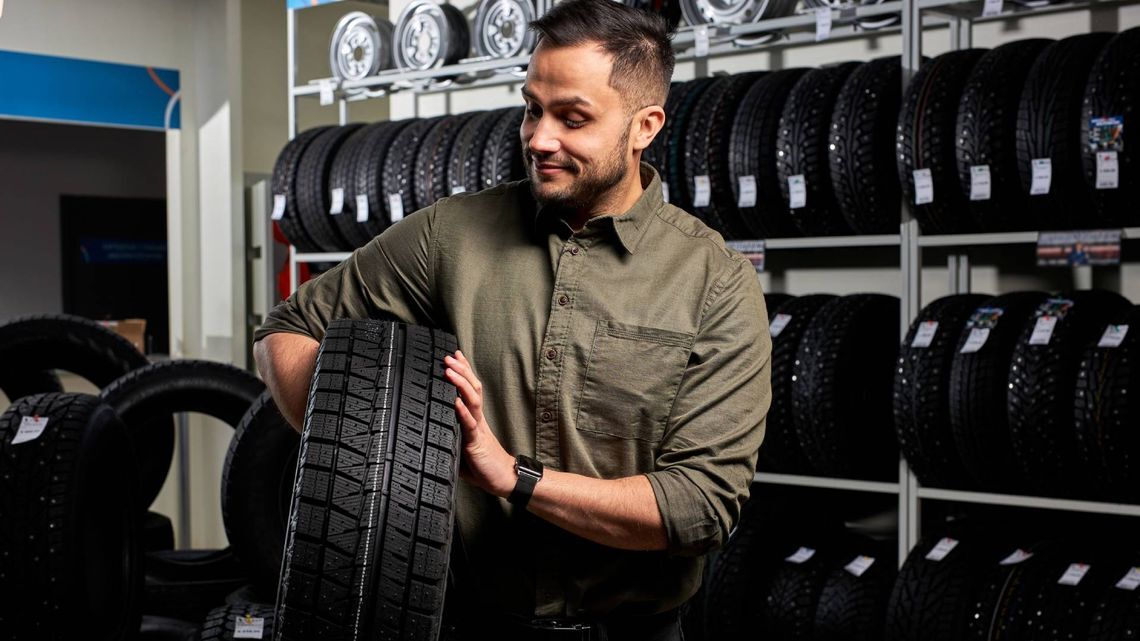 専門店でタイヤを手にする人。さまざまなサイズのタイヤが並ぶ棚に囲まれている。