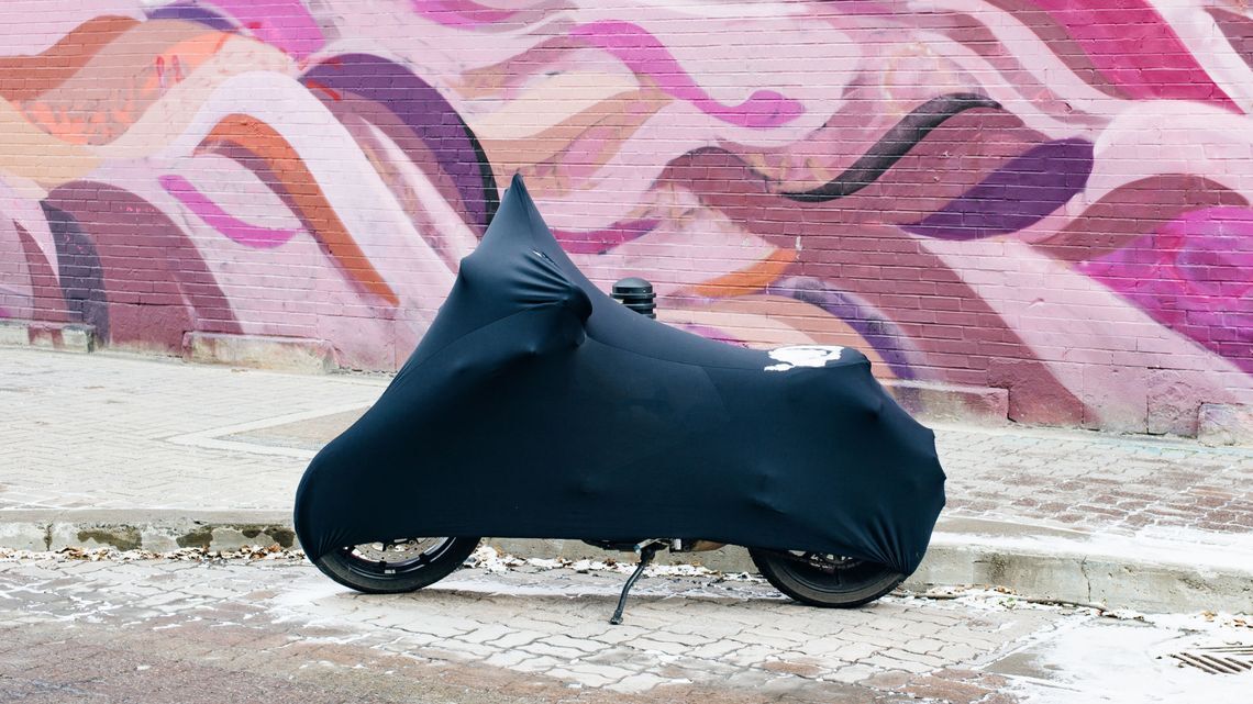 A black motorcycle is covered with a black cloth, protecting it from winter moisture and UV damage