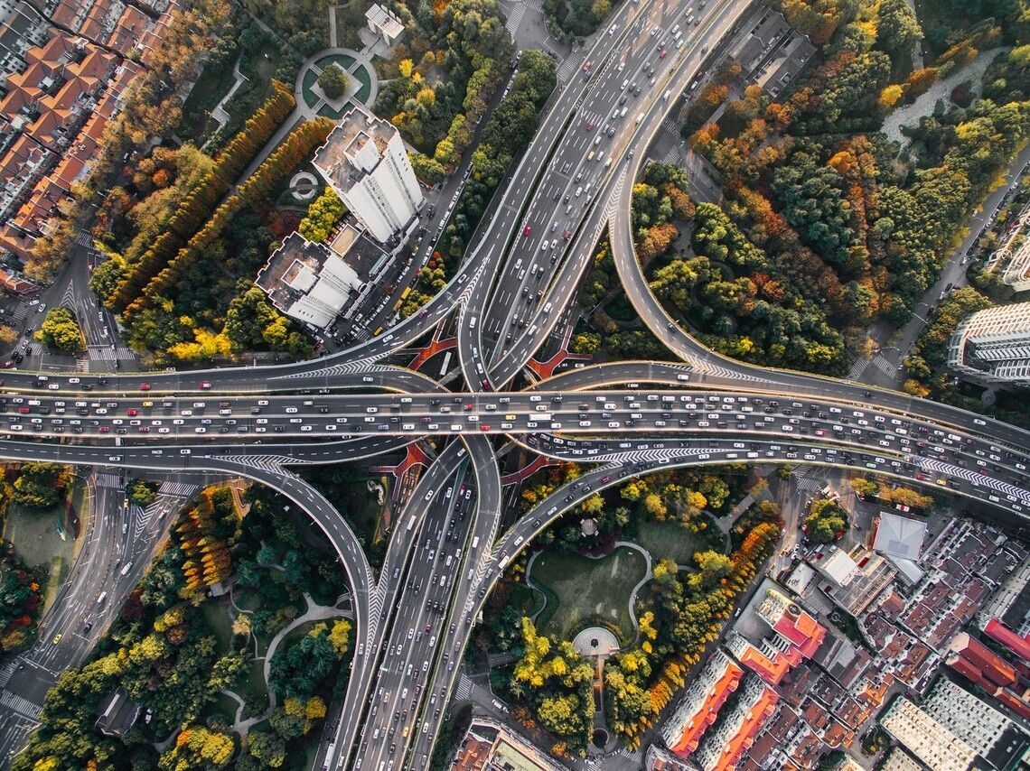 An aerial view of a highway junction in an urban area with green spaces, condos, and housing developments nearby.