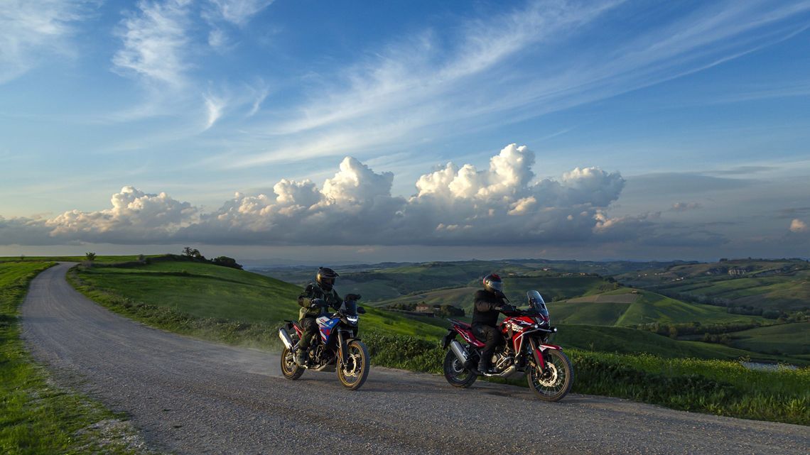 Two riders on adventure motorbikes riding down a scenic dirt road with MICHELIN Anakee Adventure 2 tyres