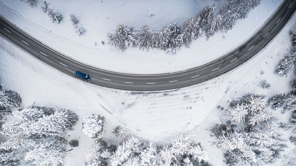 雪に覆われた森の中のワインディング・ロードと渋滞する青い車。