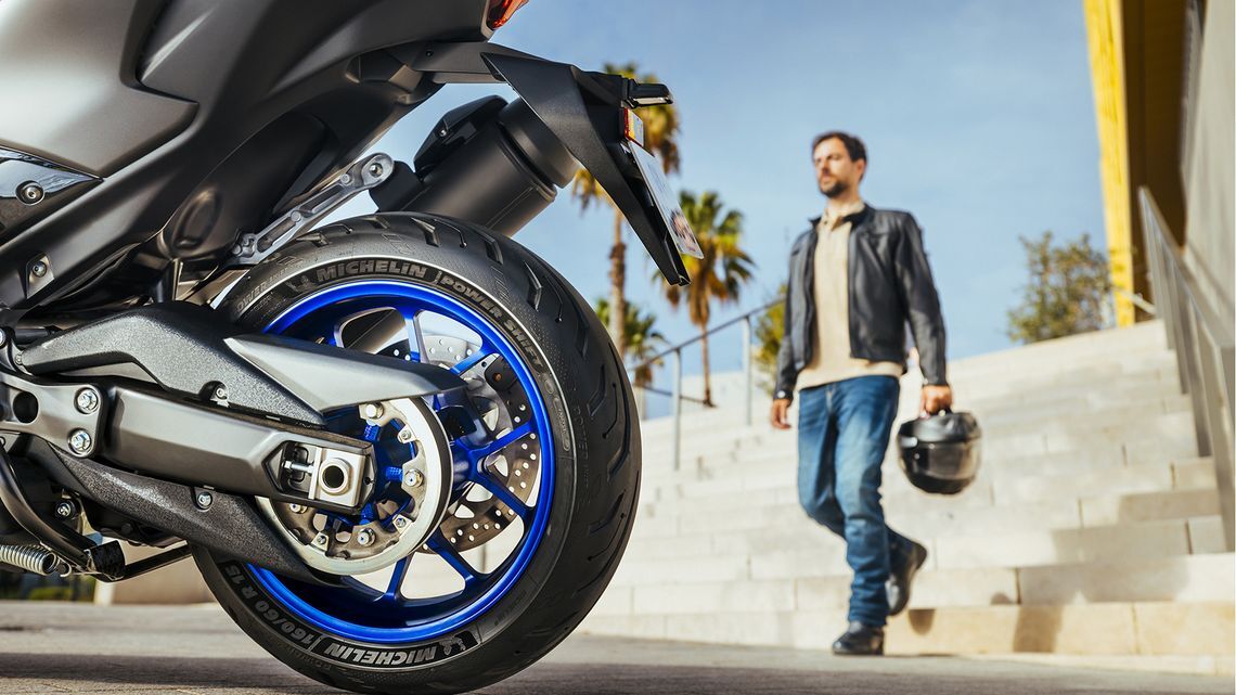 A man walks beside a motorcycle featuring striking blue rims