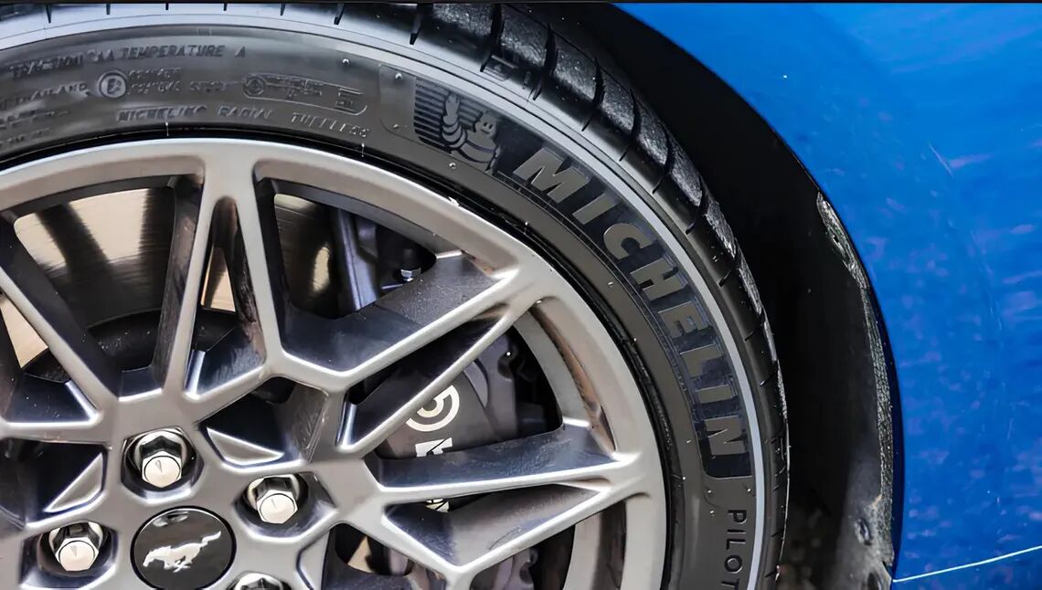 The front right section of a white car with a Michelin logo on the right door and a Michelin tyre on the right front wheel.