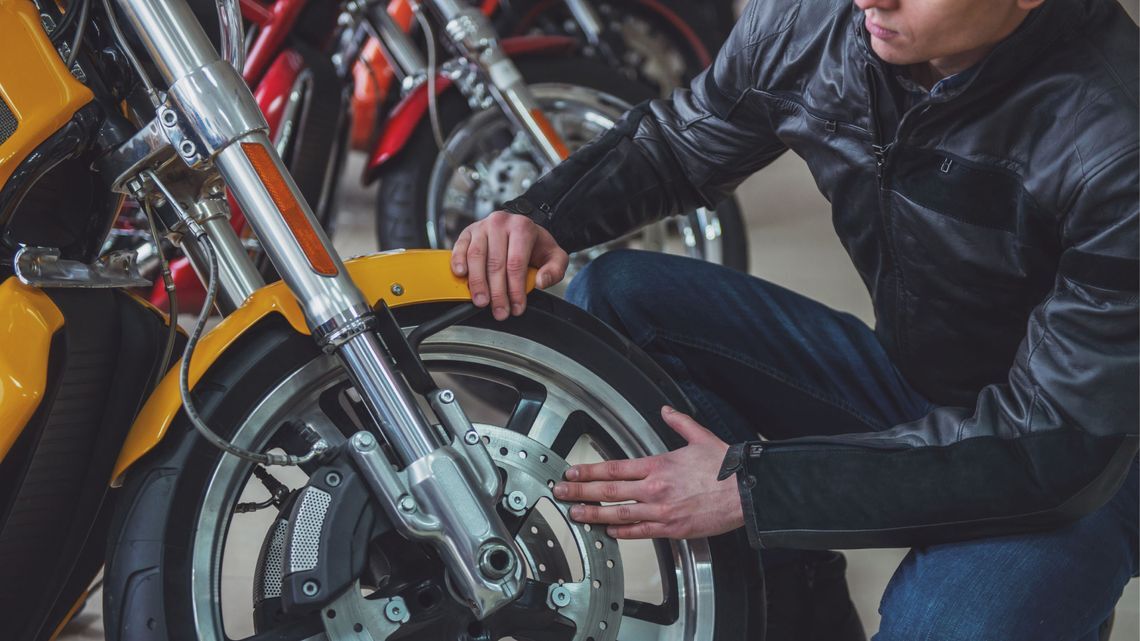 A man inspects a motorcycle tire, kneeling on the ground, concentrating on the task at hand