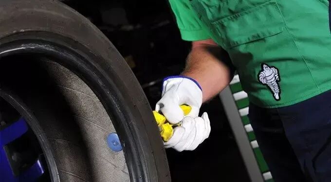 A person wearing a green Michelin uniform and white gloves checks a tire with a pressure gauge.
