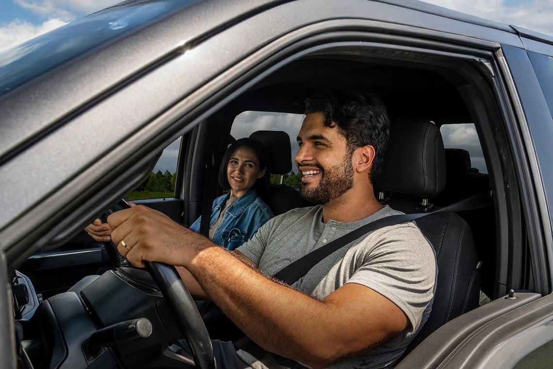 Um homem e uma mulher alegres desfrutam ambos de um passeio de carro, refletindo a alegria de explorar as suas personalidades únicas ao volante.