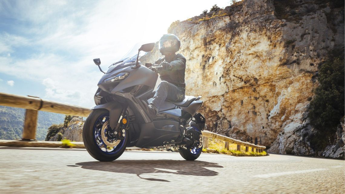 A person riding a motorcycle along a winding mountain road, surrounded by lush greenery and rocky cliffs