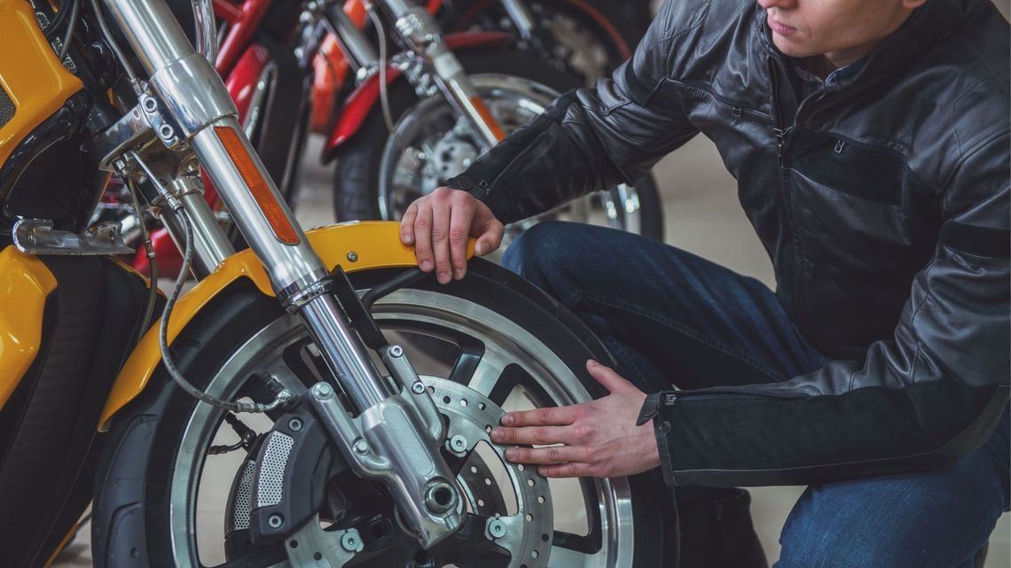 A man inspects a motorcycle tire, kneeling on the ground, concentrating on the task at hand