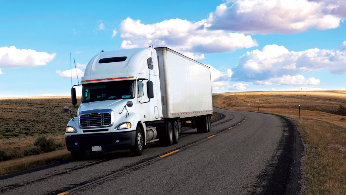 Image of white semi-truck on a highway through a scenic byway