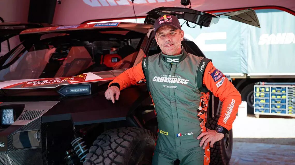 Sébastian Leob i ett tävlingsställ bredvid ett offroad-fordon under Dakar-rallyt