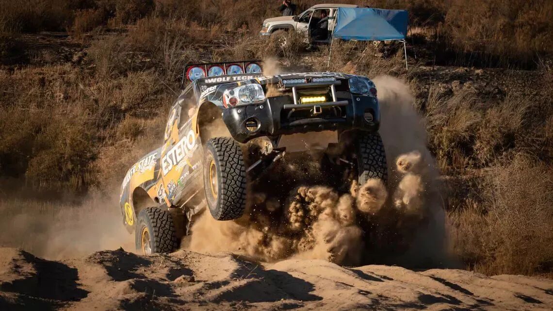 Un camión de carreras vuela sobre una duna de arena, levantando una nube de polvo durante la carrera