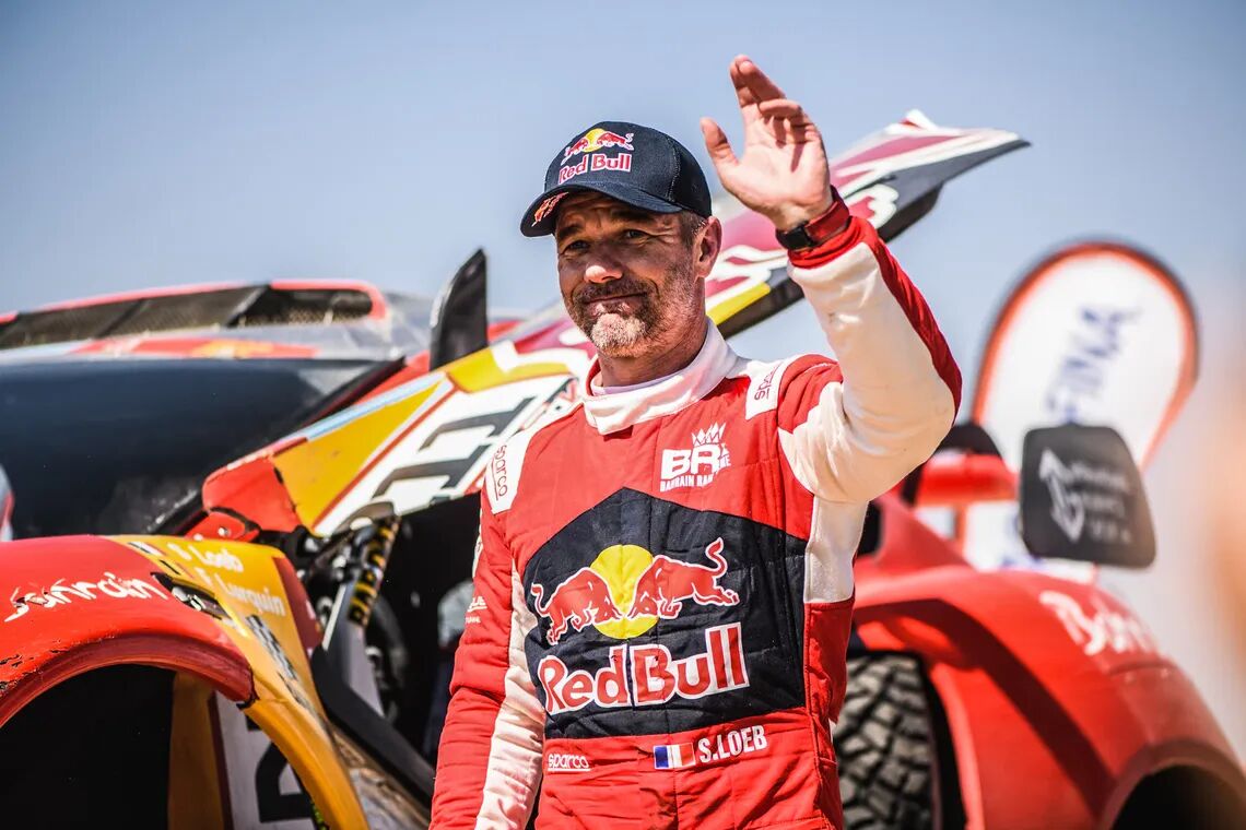 Sébastien Loeb, i ett tävlingsställ bredvid ett offroadfordon under Dakar-rallyt