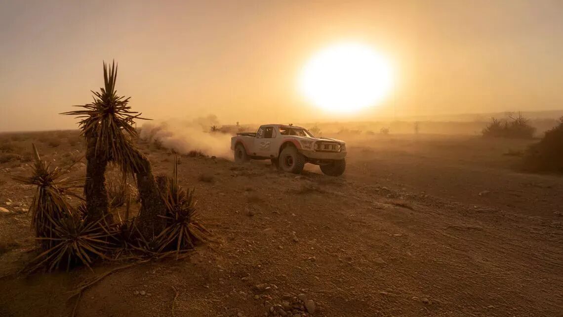 Carrera en el desierto Mint 400 al atardecer con un camión de carreras levantando polvo y plantas del desierto en primer plano