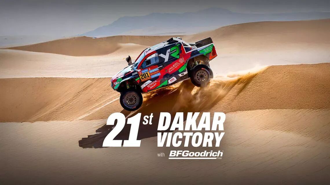 En röd, grön och svart BFGoodrich tävlingsbuggy hoppar över en sanddyn i öknen, med texten "21:a Dakar-segern med BFGoodrich-däck" skrivet över bilden.