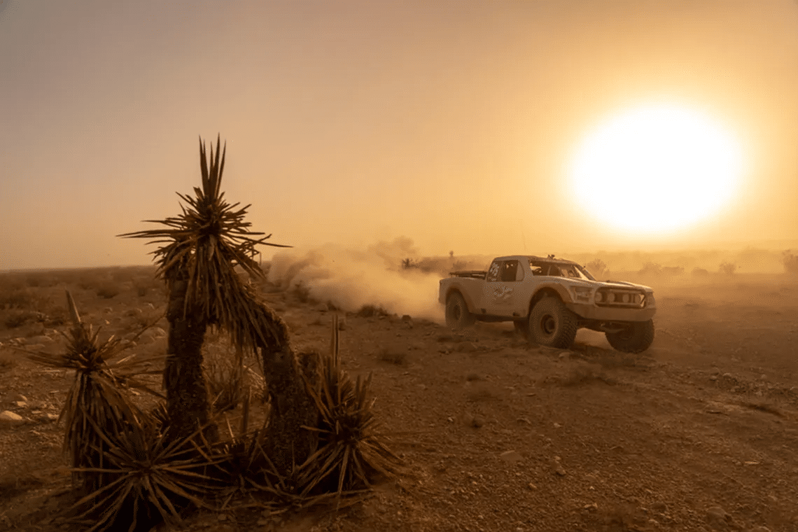 Mint 400 ökentävling i solnedgången med en tävlingslastbil som river upp damm och ökenväxter i förgrunden