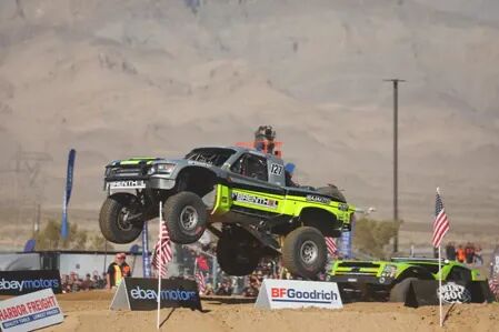 Tävlingslastbil i mitten av ett spektakulärt hopp under Mint 400-tävlingen, med amerikanska flaggor och BFGoodrich-logon i bakgrunden