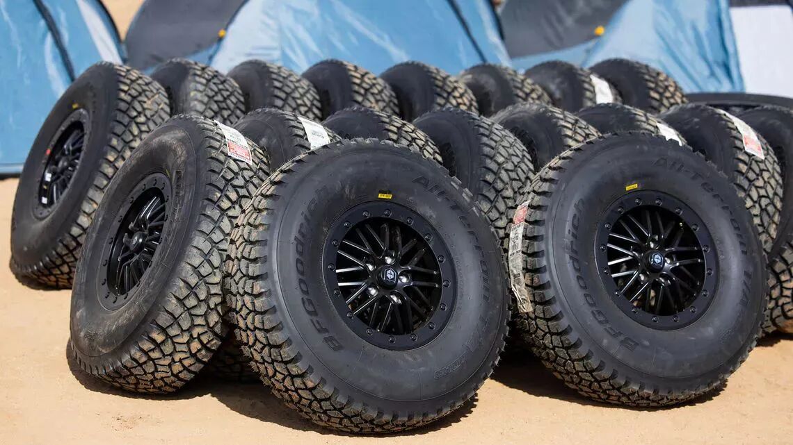 BFGoodrichs allterrängdäck med svarta fälgar staplade på sandig mark, med blå och grå tält i bakgrunden, under Dakar-rallyt