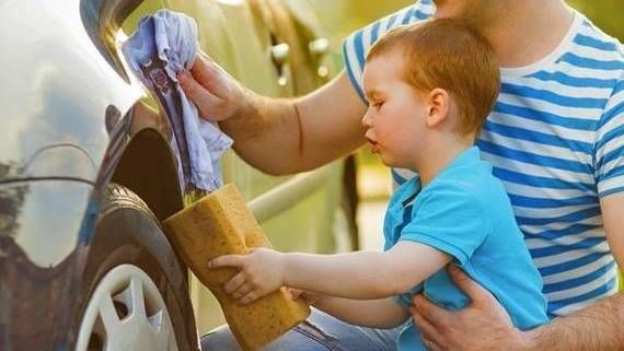 A child and a man cleaning a car tire together